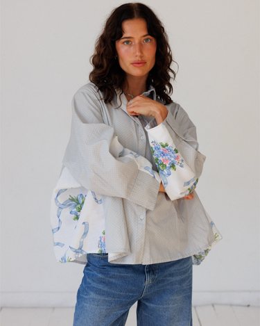 Woman wearing a light gray button up with floral cuffs and hem against a white background