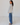 Woman wearing a light-colored blouse with floral details and blue jeans on a white floor and wall background