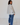 Woman wearing a light gray button-up with floral details and blue jeans on a white background