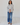 Woman wearing a light gray blouse with floral detailing and blue jeans on a white background