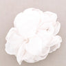 A white ruffled fabric flower accessory, likely a hair clip or decorative flower, shown on a neutral light gray background.