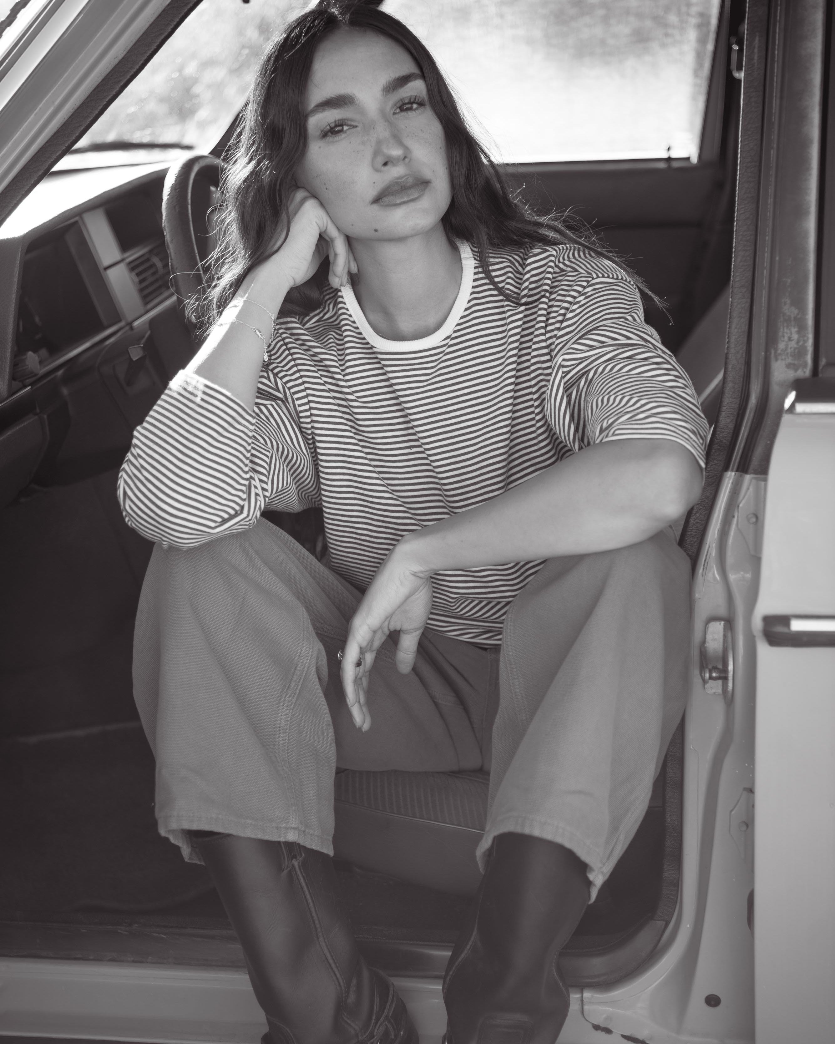 Woman sitting inside a vehicle wearing a striped shirt and knee-high boots.