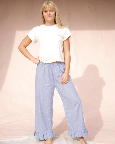 Woman wearing a white top and blue stripe casual pants with ruffled ankle hem on a plain background.
