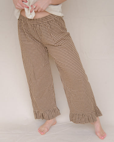 Woman wearing brown gingham casual pants with a ruffled ankle hem against a plain background.
