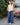 Woman in a yellow sleeveless top and blue casual pants standing next to a vintage Volvo car outdoors.