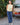 Woman in a yellow sleeveless top and blue casual pants standing next to a vintage Volvo car outdoors.