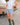 Woman in a white blouse and blue plaid boxer-style shorts standing outdoors in front of a vintage car.