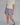 Woman wearing a pair of blue plaid boxer-style shorts with an elastic waistband and ruffle detail at the bottom, paired with a cream shirt and brown sneakers.