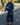 A woman wearing a dark blue denim jacket and matching wide-leg jeans, standing on an asphalt street in a residential outdoor setting.
