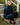A woman sits on concrete outdoor steps wearing a dark indigo denim matching set consisting of a high-neck button-front jacket and wide-leg pants, paired with brown leather loafers.