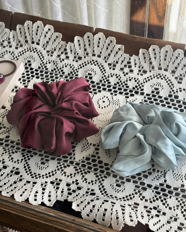 Two scrunchies, one purple and one light blue, on a lace tablecloth.