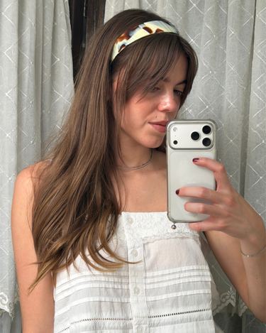 Woman taking a mirror photo of herself in a headband and white top.