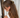 Woman with long brown hair tied back with a tortoiseshell hair clip against a white curtain background