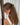 Woman with long brown hair tied back with a tortoiseshell hair clip against a white curtain background