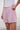Woman wearing a pair of pink plaid boxer-style shorts with an elastic waistband and ruffle detail at the bottom, paired with a white shirt.