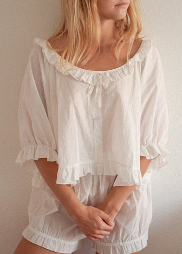 A woman wearing a white, bloomer-style shorts and a matching flowy, feminine top.