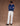 Man wearing a blue sweater with white jeans against a brown background.