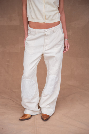 Woman wearing loose white jeans with white knee patches against a brown background.