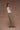 Woman wearing a white smocked top and army green military-style pants on a tan background.