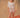 A woman wearing a white, bloomer-style shorts and a matching flowy, feminine top on a tan fabric backdrop.