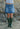 Person wearing a denim skirt and green wellington boots standing against a rocky background