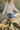 Person wearing a white cable knit sweater, blue denim skirt, and green rain boots on a rocky beach.