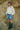 Person wearing a cream sweater, denim skirt, and green boots against a rocky background