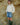 Person wearing a cream sweater, denim skirt, and green boots against a rocky background