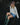 Woman sitting on a rocky surface wearing a cream sweater, denim skirt, and green wellington boots.