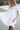 Woman in a white dress standing on a beach with waves in the background