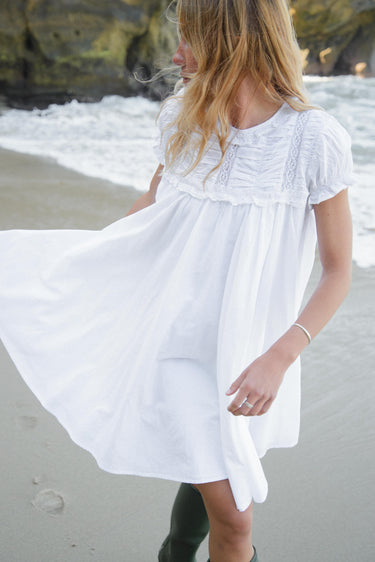 Woman in a white dress standing on a beach with waves in the background