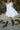 Person wearing a white dress and green boots on a beach with rocks in the background