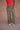 Woman wearing a red top and army green military-style pants on a tan background.