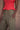 Close-up image of a woman wearing a red top and army green military-style pants on a tan background.