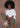 Woman sitting on a chair wearing a white t-shirt and green pants against a brown background.