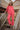 Woman standing on a wooden staircase outdoors and wearing a red blouse and pants set.