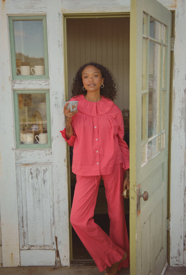 Woman standing in a doorway and holding a mug, wearing a red blouse and pants set.