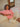 Woman sitting on a couch, wearing a pink crewneck sweater and white pants.
