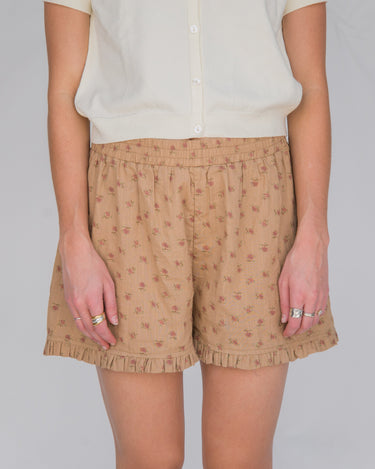 Woman wearing a pair of beige boxer shorts with a floral pattern and ruffle detail at the bottom, paired with a cream shirt.