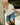 Woman in white blouse and denim shorts leaning against a wall with a blurred background