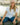 Woman sitting by a body of water wearing a white shirt, blue jeans, and green boots.