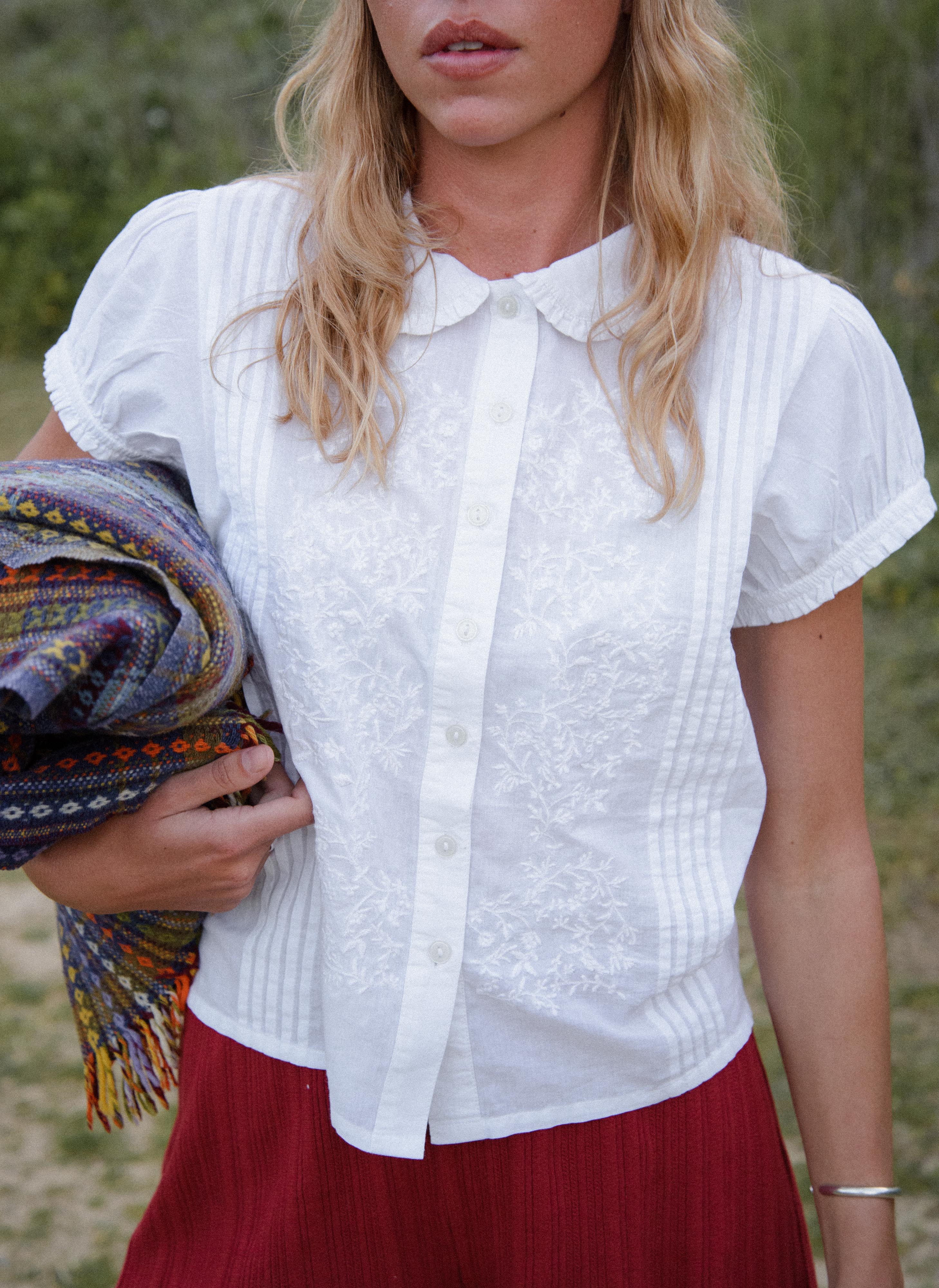 Woman wearing a white blouse and red skirt holding a colorful blanket outdoors.