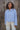 Woman standing in a field outdoors wearing a light blue wool jacket and cream pants.