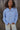 Woman standing in a field outdoors wearing a light blue wool jacket and cream pants.
