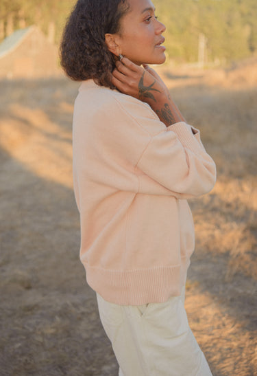 A woman wearing a blush pink sweater while standing outdoors.
