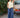 Woman in a yellow sleeveless top and blue casual pants standing next to a vintage Volvo car outdoors.
