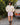 Woman in a cream cable knit sweater and pink plaid boxer-style shorts standing outdoors next to a vintage Volvo car.