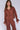 A woman standing in front of a white background wearing a brown top with a sailor-style collar and matching brown pants with an elasticated waistband and cuffed hems. The outfit features drawstrings and the top is tied at the front.