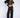 Woman wearing a black, rolled hem sweater and matching black sweater pants on a white fabric background.