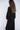 Woman wearing a black, rolled hem sweater and matching black sweater pants on a white fabric background.